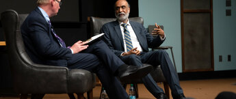 Two men sitting on tables on a stage talking to each other