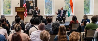 Two men sitting on a stage talking in front of a crowd