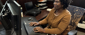 Asenath Asha Lutabingwa working at her computer