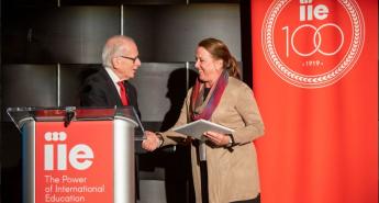Carol Strange shaking hands at a podium with Allan Goodman, CEO of the Institute of International Education