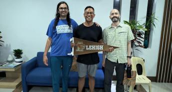 Three people smiling for the camera, with one holding a Lehigh University flag