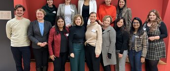 A group of people standing in front of a red wall, smiling for a photo