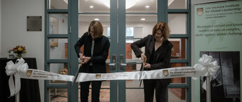 Two women cutting a ribbon at a ribbon-cutting event in an office setting