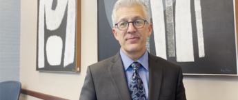 A man wearing glasses and a gray suit with a blue shirt and tie staring at the camera