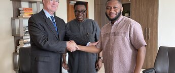 Two men shaking hand and smiling for the camera as another smiling man stands behind them