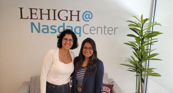 Two women stand in front of a Lehigh@NasdaqCenter logo