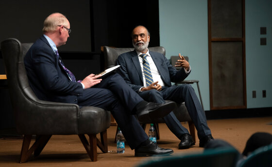 Two men sitting on tables on a stage talking to each other