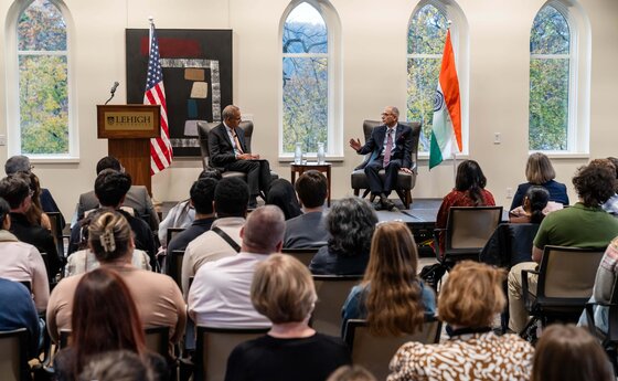 Two men sitting on a stage talking in front of a crowd