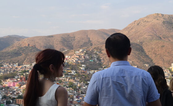 A person in the foreground taking a selfie of himself and several young people sitting at a table under an outdoor canopy