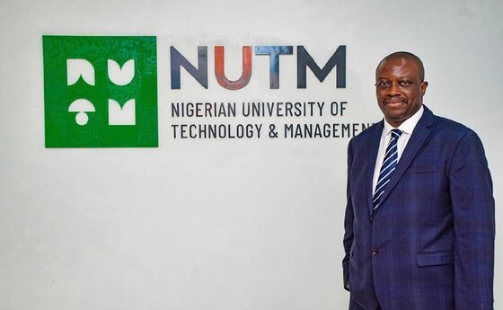A man standing in front of the logo for the Nigerian University of Technology and Management (NUTM)