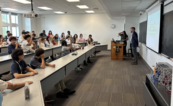 Students in a classroom listening to speakers standing by a podium
