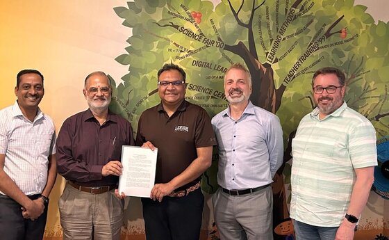 Five men posing for a photo while two of them hold up a written agreement