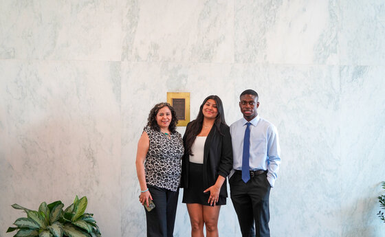 Three people posing for a photo in front of a marble wall