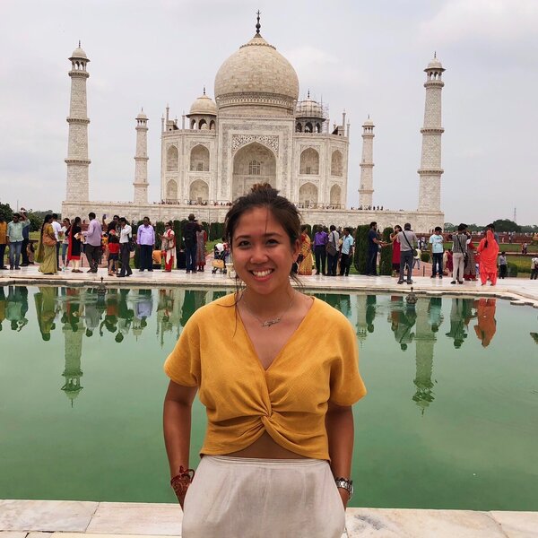 A woman standing in front of a reflective pool with the Taj Mahal in the background